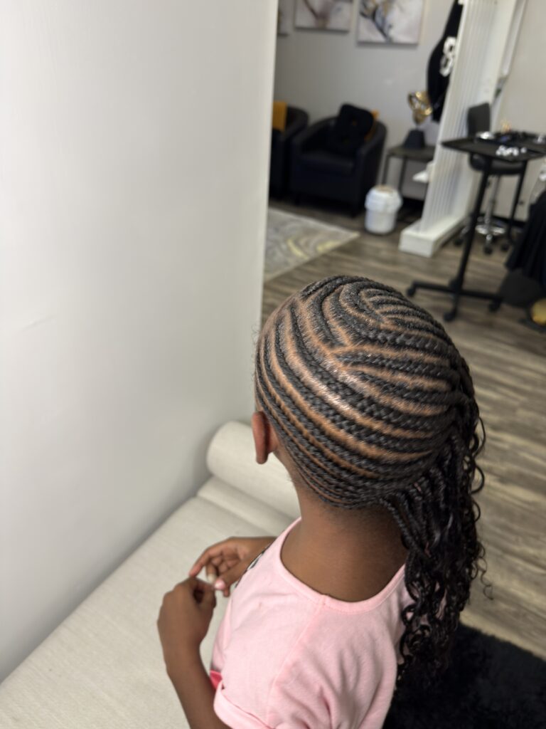 Side view of a young girl receiving intricate braids at Nerielle Braiding Studio