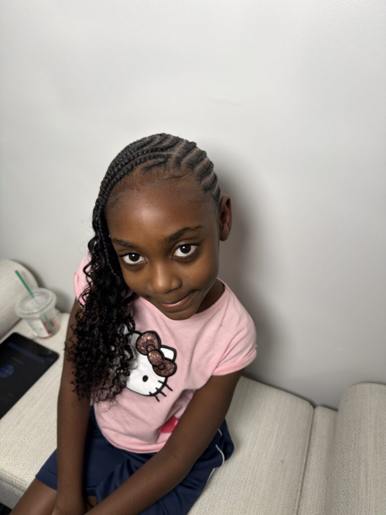 Smiling young girl with intricate braided style, photographed at Nerielle Braiding Studio