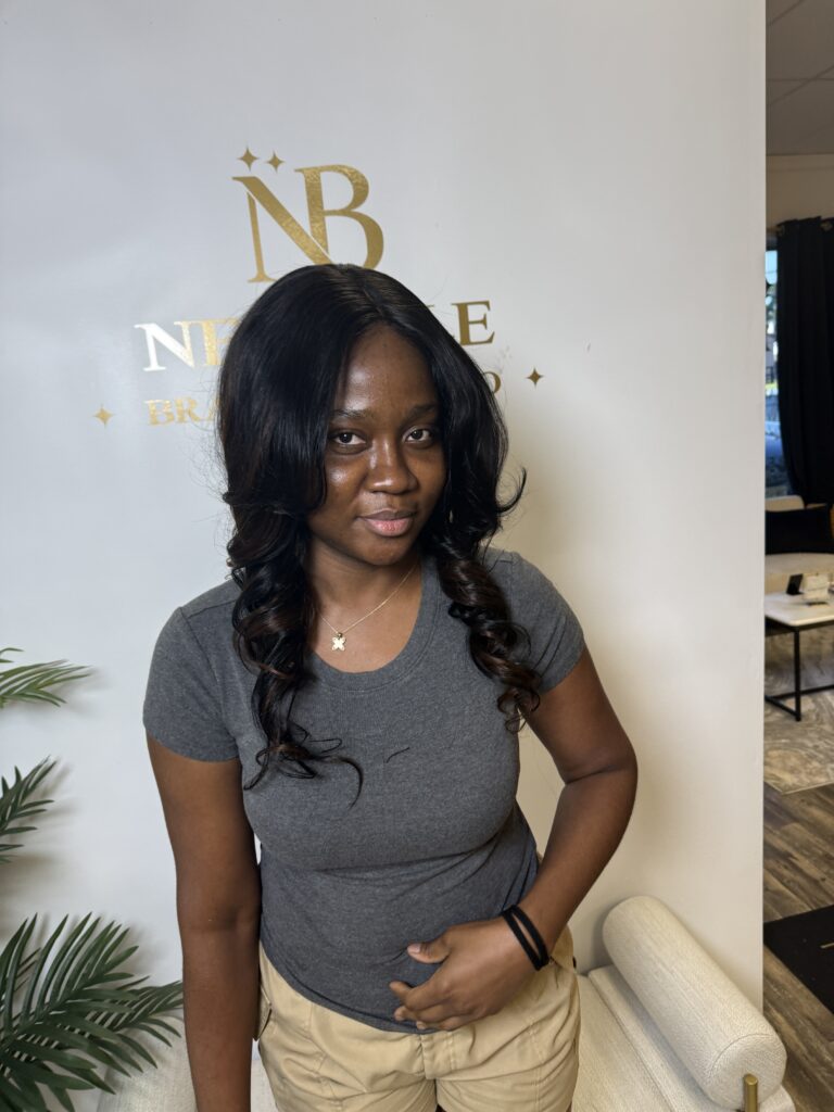 Smiling woman with a wavy sew-in weave installation, photographed at Nerielle Braiding Studio